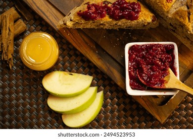 A delicious slice of fruit bread topped with vibrant berry jam is showcased on a wooden cutting board. Accompanying the bread is a jar of honey, fresh green apple slices, and a bowl of rich berry jam. - Powered by Shutterstock