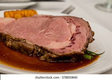 A Delicious Slice Of Medium Rare Prime Rib On A White Plate With Gravy Or Au Jus