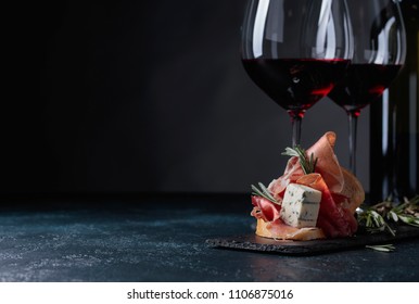 Delicious Snack And Glasses Of Red Wine. Sandwich With Prosciutto, Blue Cheese And Rosemary On A Dark Background.  Copy Space For Your Text.
