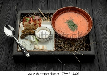 Delicious soup served with bread and side dishes on wooden table. Soup is served in a bowl with bread, pickles, and yogurt on a wooden table.