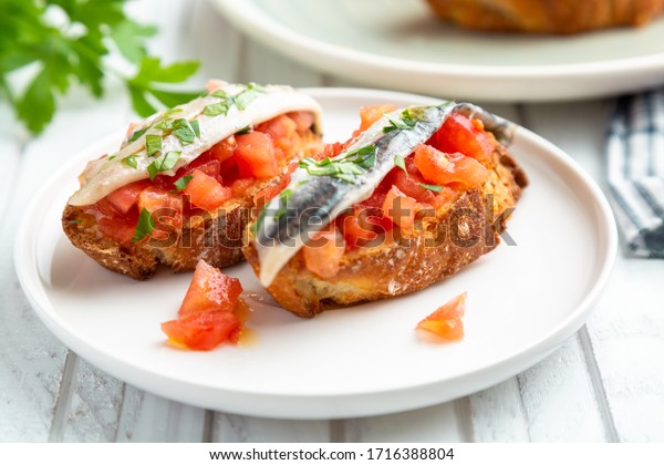 Delicious spanish tapa with marinated anchovies in\
vinegar, fresh tomato, olive oil and parsley on slices of toasted\
bread