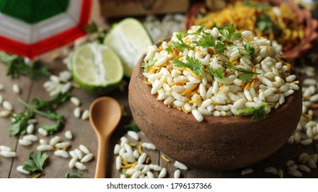 delicious, spicy Bengali snacks, Jhalmuri, is served in an earthen bowl placed on a wooden table with other ingredients like lemon being spread around it.
