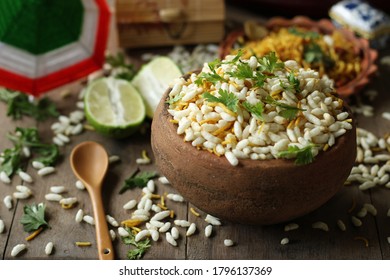 delicious, spicy Bengali snacks, Jhalmuri, is served in an earthen bowl placed on a wooden table with other ingredients like lemon being spread around it.