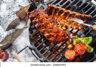 Delicious spicy marinated spare ribs grilling over a winter BBQ outdoors alongside a woodpile covered in fresh snow