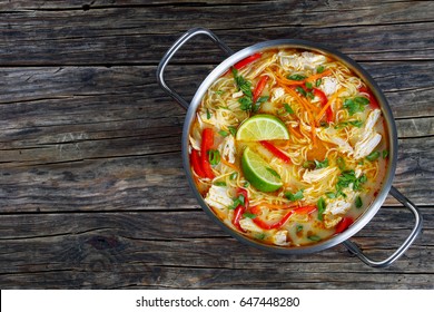 Delicious And Spicy Thai Chicken Noodle Soup In Cooking Pot On Old Dark Wooden Table, Traditional Classic Recipe, View From Above