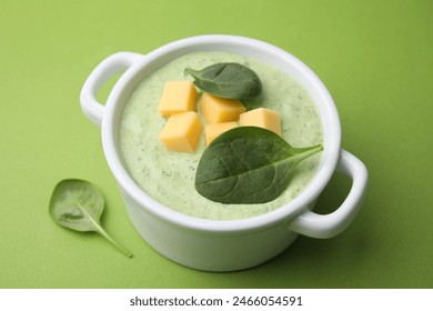 Delicious spinach cream soup with cheese in bowl on green background