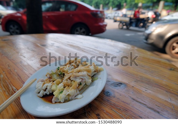 The delicious\
Steamed Vermicelli Roll is a street food in southern China and Hong\
Kong. It is placed on the table with chopsticks, and the background\
is blurred road traffic.