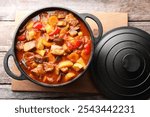 Delicious stew with vegetables in pot on wooden table, top view