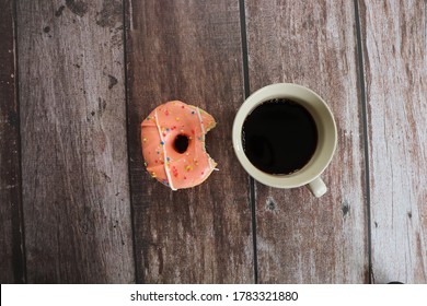 A Delicious Strawberry Flavour Donut With Bite Mark And A Coffee Cup On Wooden Background