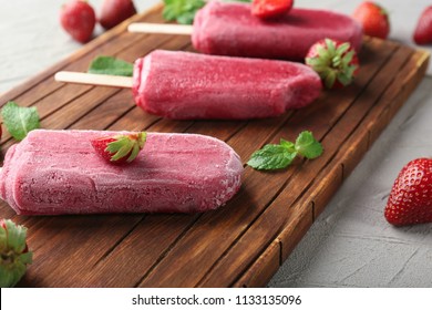 Delicious strawberry popsicles with berries on wooden board