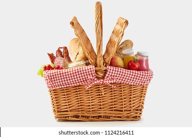 Delicious summer picnic food in a wicker hamper with crusty bread, fresh fruit and juice, cheese and tomatoes side on isolated on white