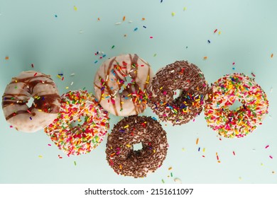 A Lot Of Delicious Sweet Donuts In Frozen Flight On A Light Blue Background. Holiday, Sweet Food, Romantic Date. There Are No People In The Photo. Advertising, Birthday Invitation.