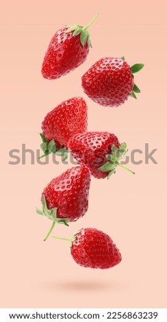 Delicious sweet strawberries falling on pale pink background