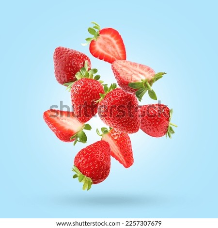 Delicious sweet strawberries falling on light blue background