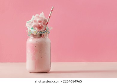 Delicious sweet strawberry milkshake in a glass jar, topped with a cotton candy on pink background