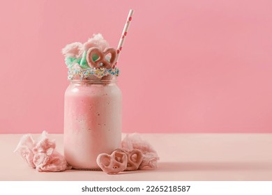 Delicious sweet strawberry milkshake in a glass jar, topped with a cotton candy and pink pretzel