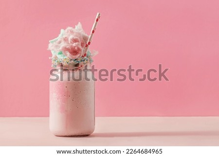 Delicious sweet strawberry milkshake in a glass jar, topped with a cotton candy on pink background