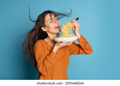 Delicious taste. Beautiful young girl eating delicious Italian pasta isolated on blue studio background. Holidays, traditions, food, popularity, cafe, love. Healthy carbohydrates. Copy space for ad