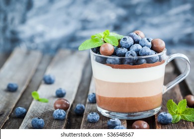 Delicious  Three Layered Chocolate Mousse Dessert, Decorated With Fresh Blueberry, Mint And Candies, Served In Glass Cup