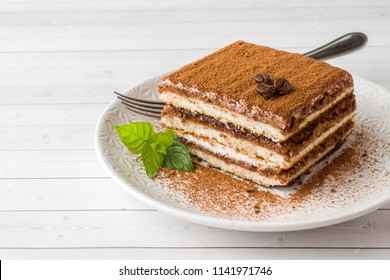 Köstlicher Tiramisu Kuchen mit Kaffeebohnen und frischer Minze auf einem Teller auf hellem Hintergrund.