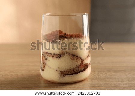 Delicious tiramisu in glass on wooden table, closeup
