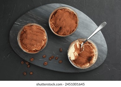 Delicious tiramisu in glasses, spoon and coffee beans on black table, top view - Powered by Shutterstock