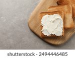 Delicious toasted bread slices with cream cheese on grey textured table, top view. Space for text