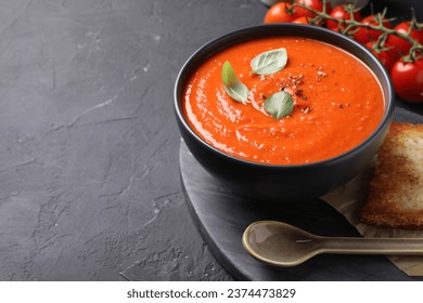 Delicious tomato cream soup served on black textured table. Space for text