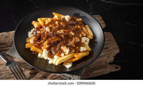 Delicious traditional canadian dish poutine gravy and fries with cheese curd in dark environment