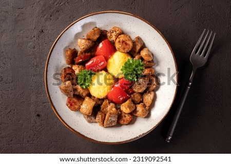 Delicious traditional romanian dish pomana porcului assortment of pork meat and sausages with mamaliga and pickled red peppers in a plate on dark background. Top view.