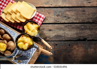 Delicious traditional Swiss melted raclette cheese on diced boiled or baked potato served in individual skillets, overhead view on rustic wooden table with copy space