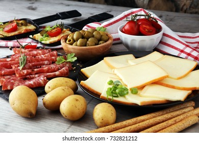 Delicious traditional Swiss melted raclette cheese on diced boiled or baked potato served in individual skillets with salami.