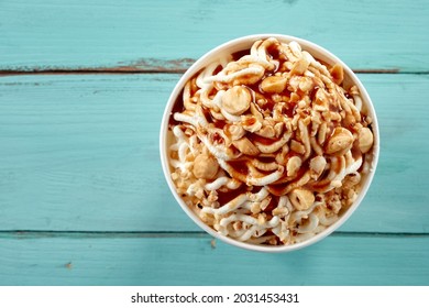 Delicious Trendy German Vanilla Spaghetti Ice-cream Sundae Topped With Fresh Hazelnuts And Caramel Sauce In A Close Up Top Down View Over Blue Wood With Copyspace For Menu Advertising