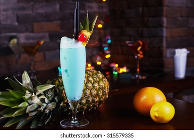 Delicious tropical blue curacao alcoholic cocktail garnished with a fresh pineapple slice and maraschino cherries on a table in the restaurant with background of beautiful disco lights. soft focus