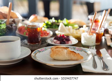 Delicious Turkish and Arabic Traditional Rich Sunday Breakfast serving with Puff Borek, Feta Cheese, Tomato, Avocado Salad, Black Tea, Green Olive, Hot Coffee, Beef Ham and Cherry Jam on wood table.