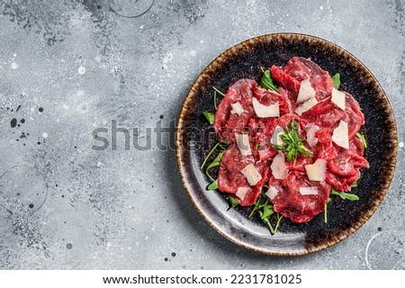 Delicious veal carpaccio with Parmesan cheese, spices and herbs. Gray background. Top view. Copy space.