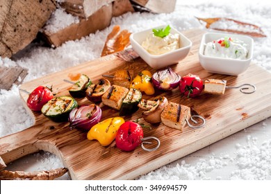 Delicious vegetarian winter barbecue with assorted vegetables and tofu or bean curd on skewers and grilled corn on the cob served on a wooden board outdoors in winter snow