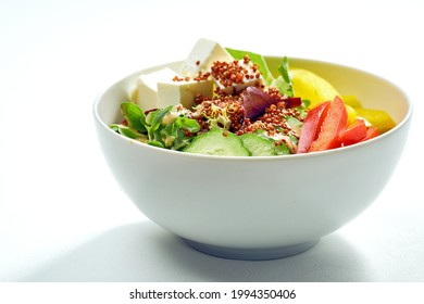 Delicious veggie bowl with cucumber, bell pepper, salad mix, quinoa and tofu in a white plate. Isolated on grey background.