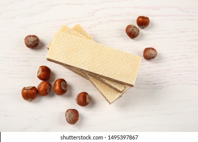 Delicious wafers with hazelnuts on white wooden background
