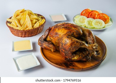 Delicious whole grilled chicken with french fries, salad and creams on wooden plate. Peruvian food "pollo a la brasa con papas fritas". White background. - Powered by Shutterstock