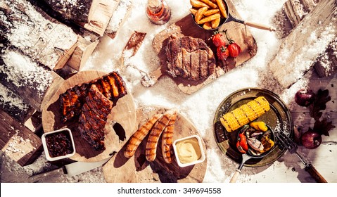 Delicious winter barbecue spread with assorted grilled marinated meat and vegetables served outdoors in the snow, overhead view
