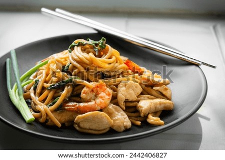 Delicious yakisoba noodles stir-fried with basil and dried chillies. Stir-fried with oyster sauce, soy sauce and chicken fillet, shrimp, decorated with scallions on a black plate. Home cook