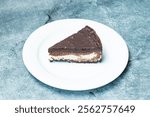 A deliciously rich and creamy nutella oreo cheesecake slice is placed elegantly on a while plate with a minimalistic background.