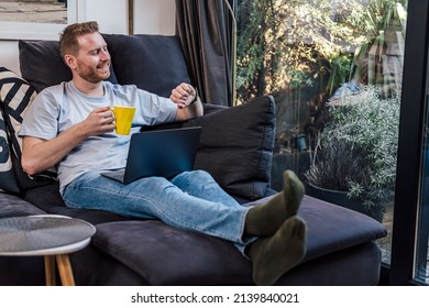 Delighted adult man, looking at his watch, drinking tea and working from home.