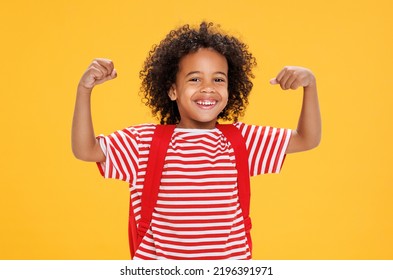 Delighted African American boy schoolkid student laughs and  shows strong muscles while having fun during school  against yellow background - Powered by Shutterstock