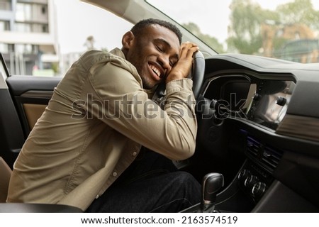 Delighted African American man hugging the steering wheel of his new car, closing his eyes and smiling