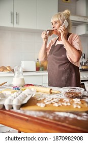 Delighted Aged Woman Having A Phonecall While Sipping Tea In Her Homely Kitchen