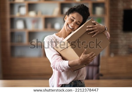 Delighted attractive young woman customer hugging paper box parcel with closed eyes and smiling, home office interior, copy space. Parcel mail delivery, courier service concept