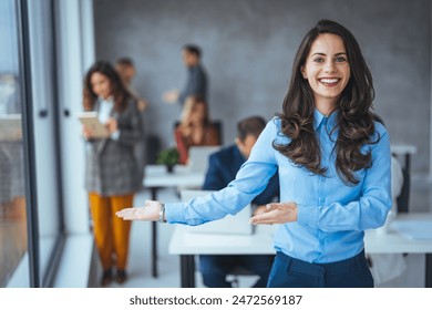 A delighted Caucasian businesswoman with open arms ready for teamwork stands in a bustling, well-lit workspace, her professional attire reflecting her executive role - Powered by Shutterstock