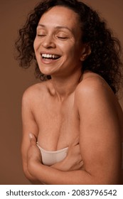 Delighted confident dark-haired curly woman with closed eyes and skin flaws in beige underwear smiles toothy smile posing against beige background with copy space for ads